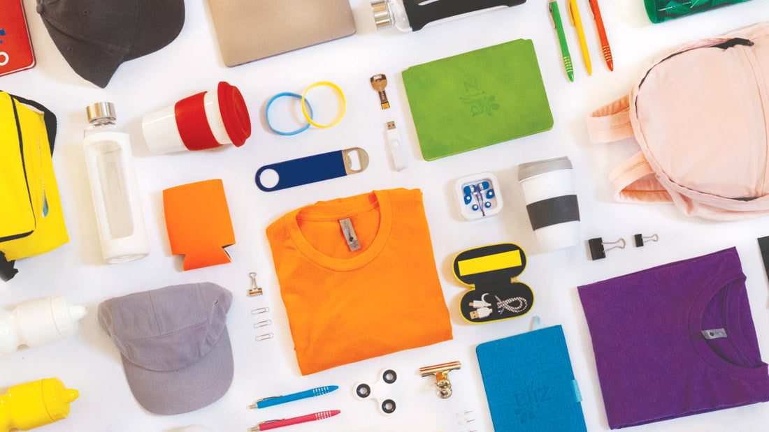 Collection of promotional products including t-shirts, hats, and keychains on a white surface.